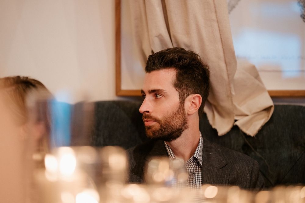 A guest listens intently during an intimate dinner gathering under soft lighting.