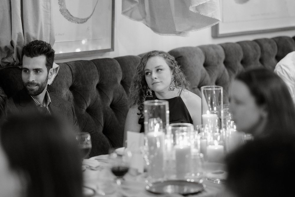 Guests engage in conversation at an elegant restaurant table with ambient candlelight.
