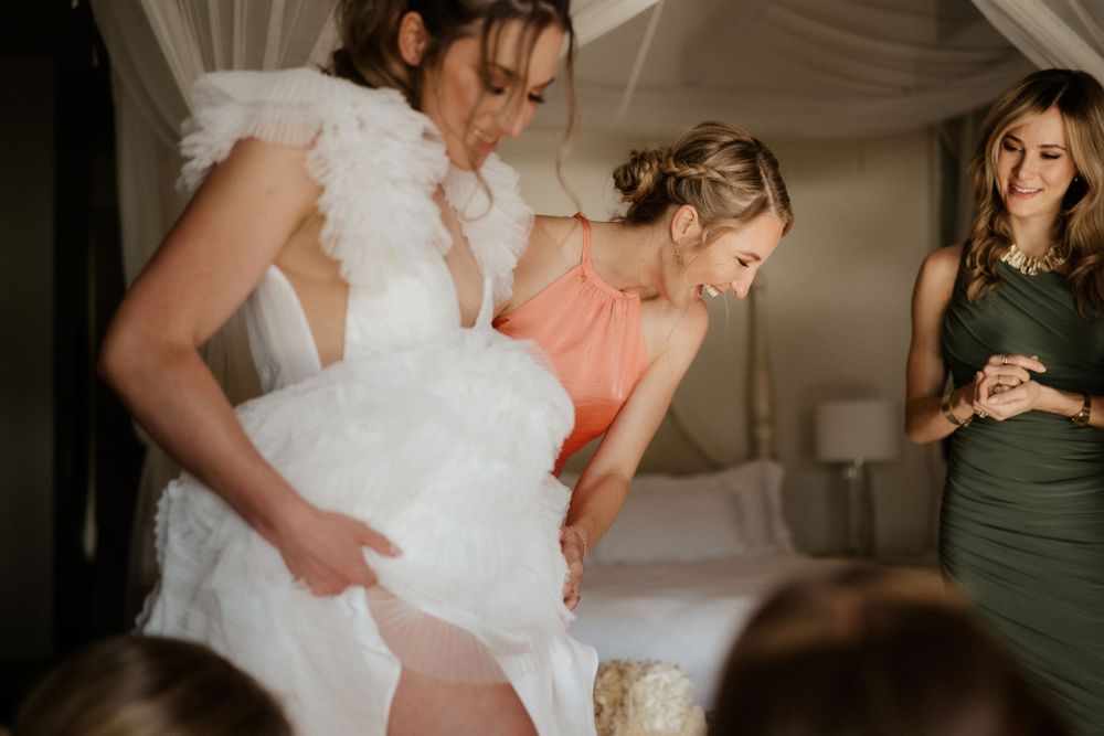 Bridal preparation moment captured in elegant room with chandelier and flowing curtains.