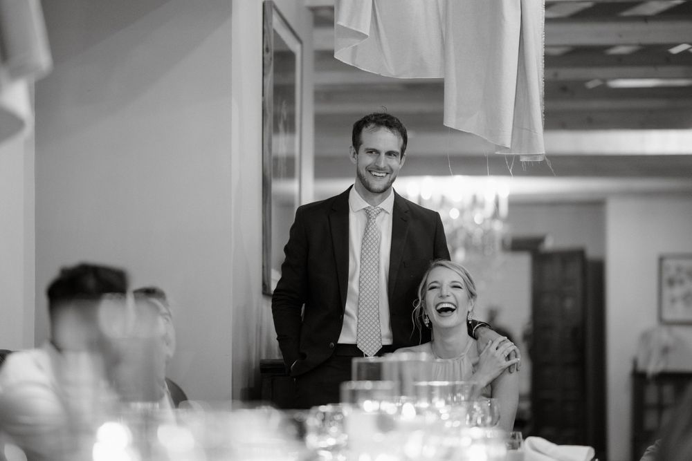 Black and white candid moment of guests laughing during wedding reception speeches.