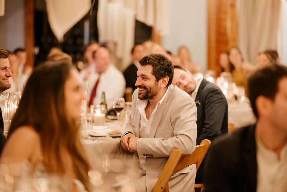 Wedding reception guests enjoying dinner and conversation at tables with warm lighting.