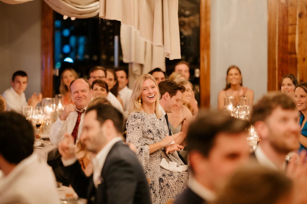 Wedding reception guests laugh and smile while seated in an elegant venue with draping decor.