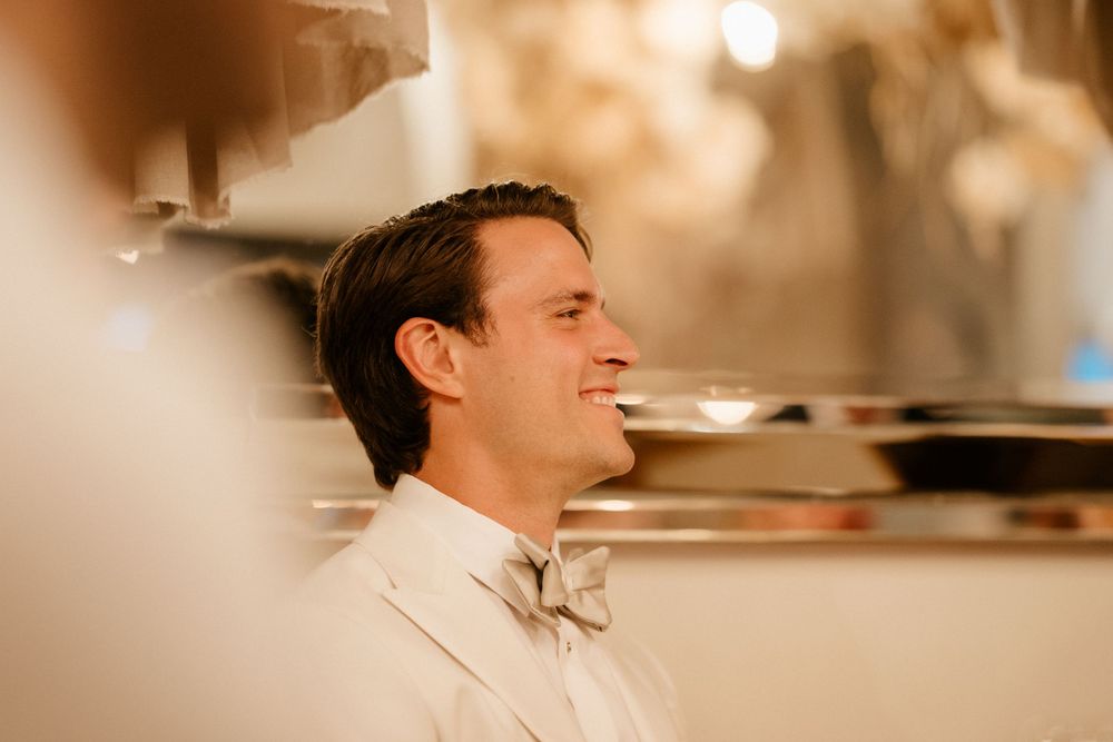 Side profile of a groom smiling during an elegant indoor wedding celebration.