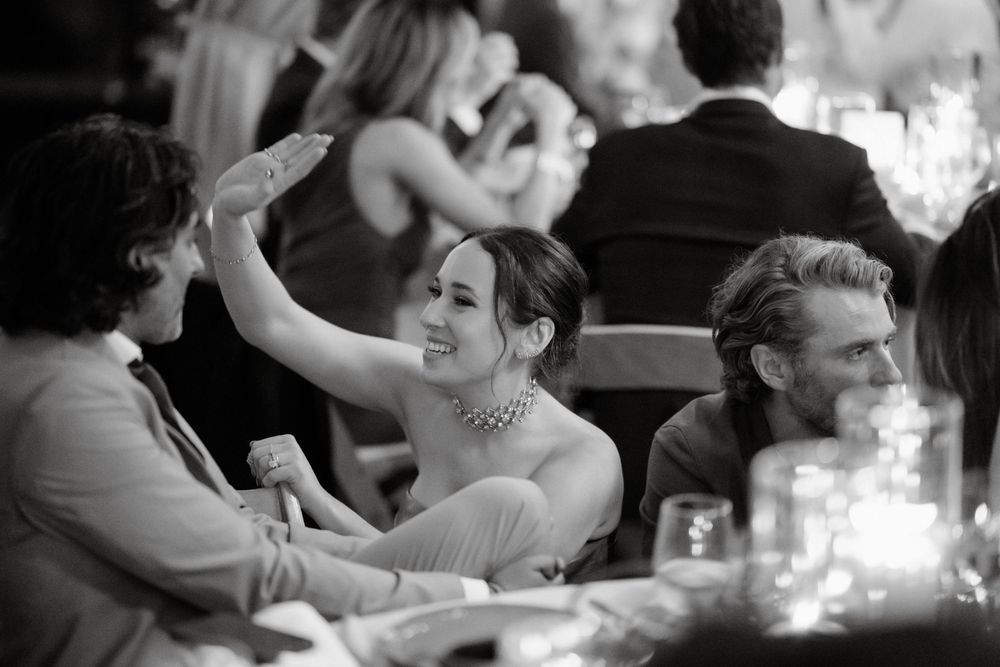 Black and white candid reception photo showing guests celebrating at elegant dinner tables.