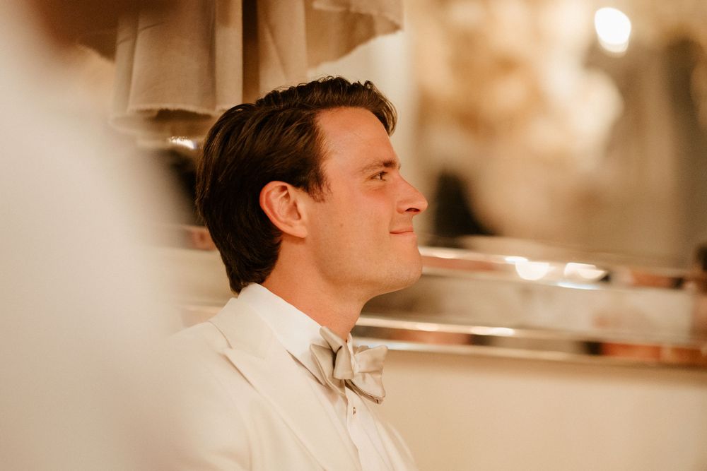 Profile view of a groom in a white bow tie and suit at an elegant reception.