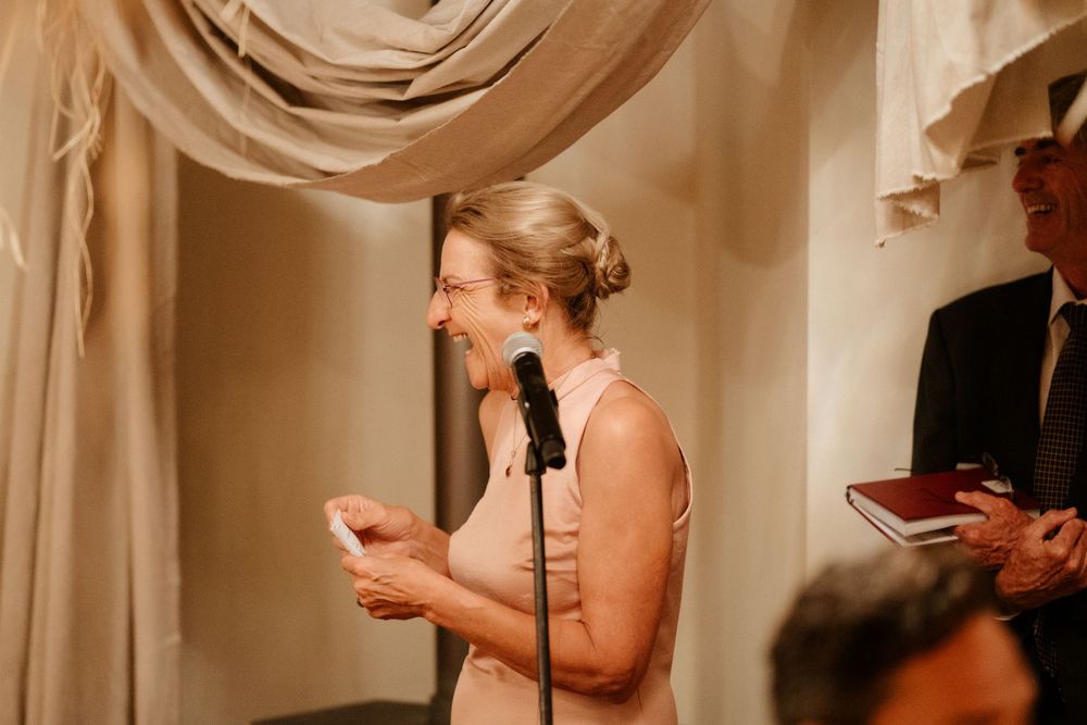 Person giving speech at wedding reception with elegant draped fabric decor.