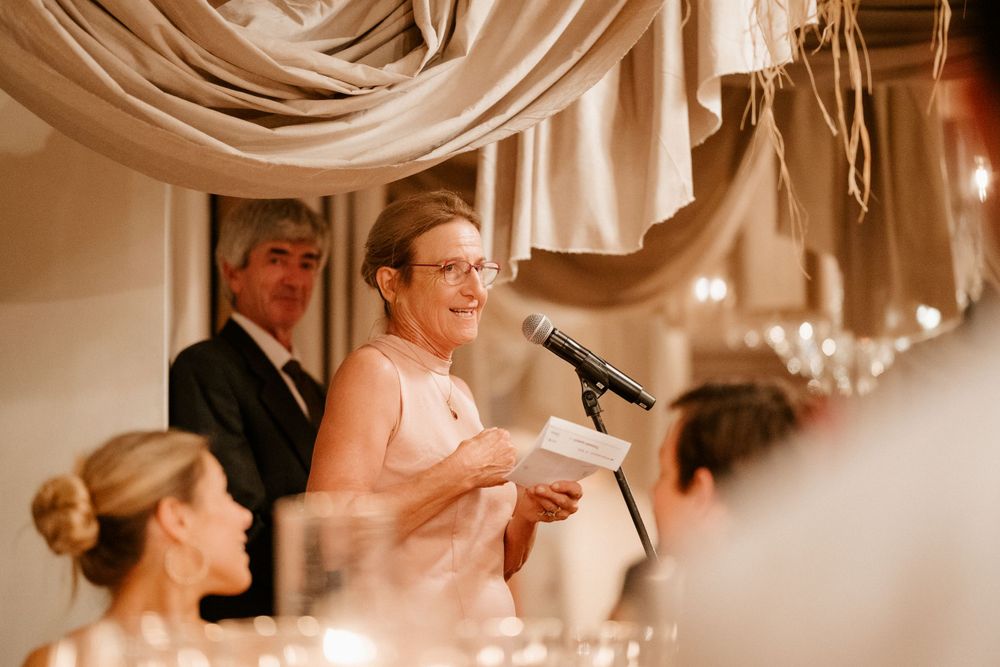 Wedding reception speech being given in an elegantly decorated room with draped fabric and chandeliers.