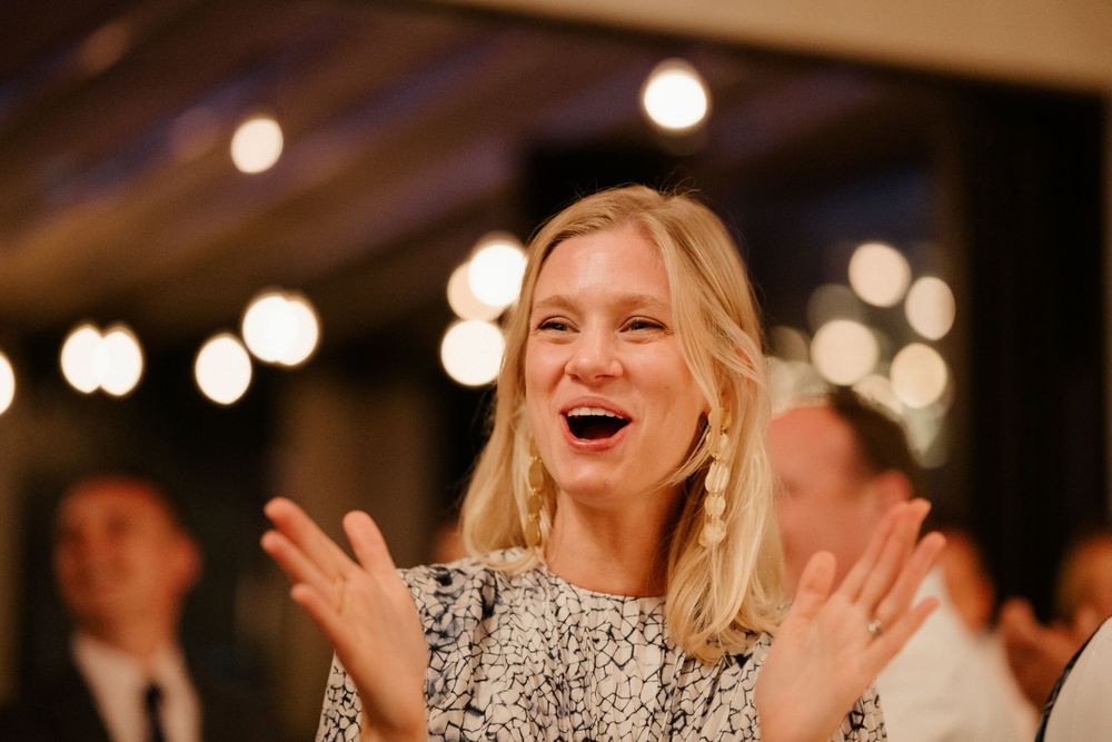 Wedding guest in sparkly dress laughs joyfully under ambient lighting.