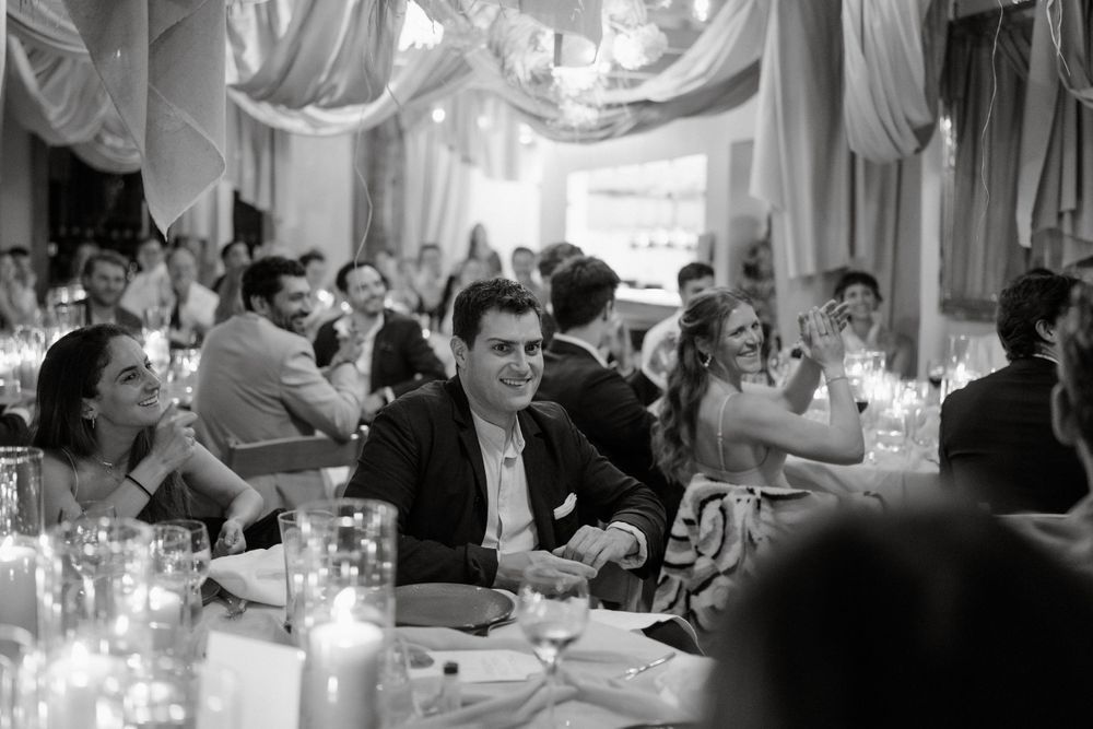 Black and white photo of wedding reception guests dining at elegantly decorated tables with candlelight.