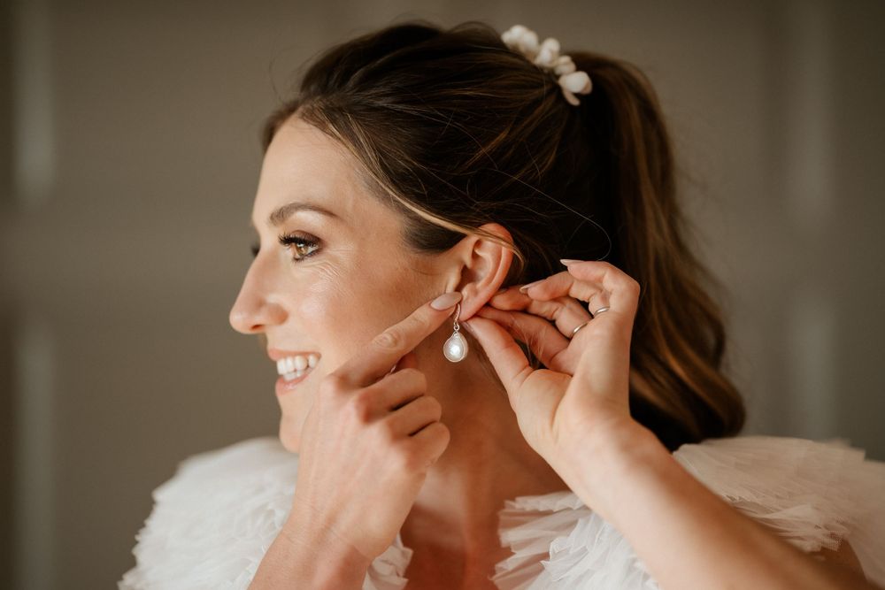 Close-up shot of someone putting on earrings during wedding preparation.