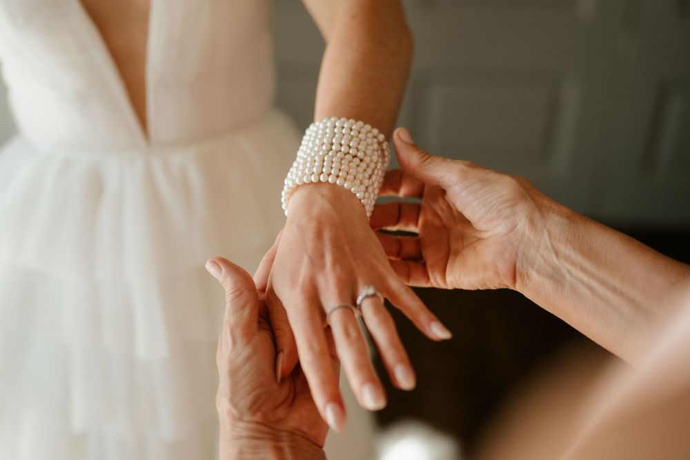 Close-up of pearl bracelet being placed on wrist over white dress fabric.