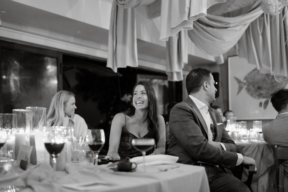 Black and white photo of wedding guests enjoying dinner at elegant reception.