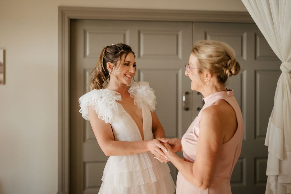Two women share an emotional moment during wedding preparations in a sunlit room.