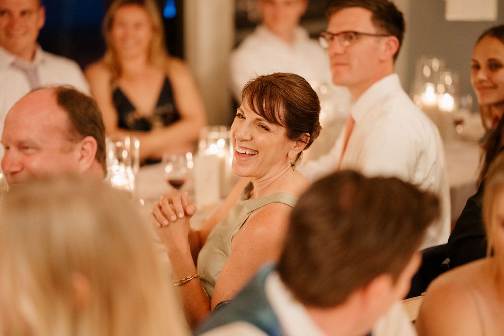 Wedding guests laughing joyfully during an indoor reception celebration with warm lighting.