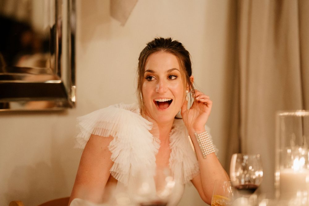 A bride in a feathered white dress expressing excitement during the wedding reception.