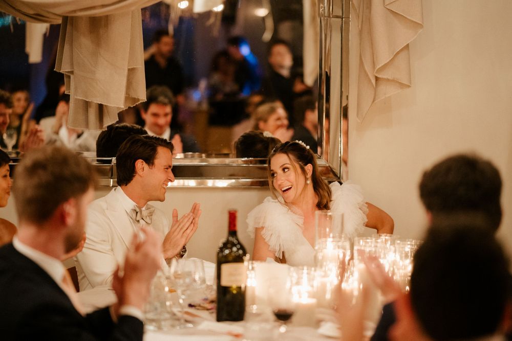 Wedding guests enjoying animated conversation at a candlelit reception dinner.