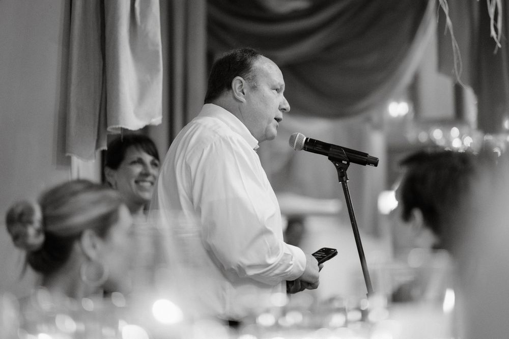 A speaker delivers remarks at a wedding reception with candles on tables in black and white.