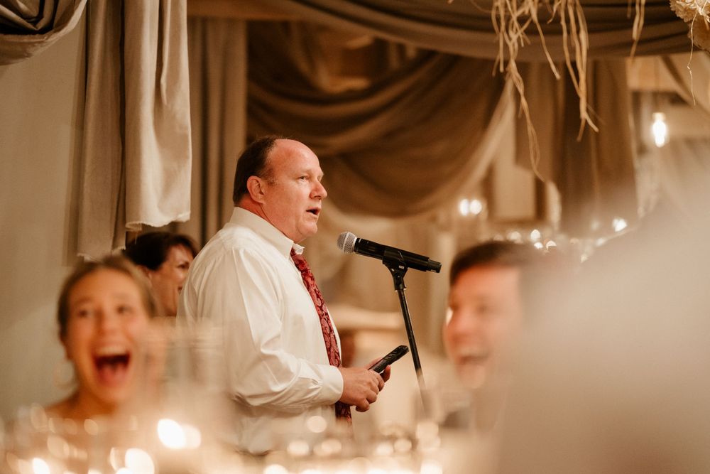 Wedding reception speaker delivers emotional toast at candlelit venue.