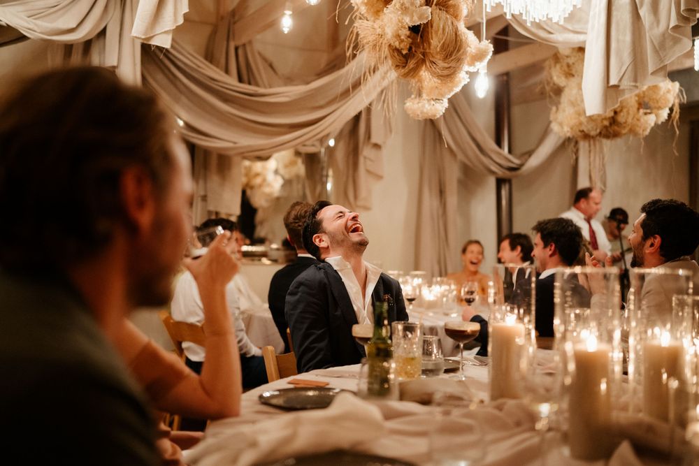 Laughter fills the elegant reception hall as guests dine under ornate draped ceiling and chandeliers.