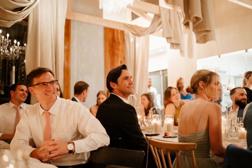 Wedding guests seated at elegant reception tables with soft lighting and hanging decorations.