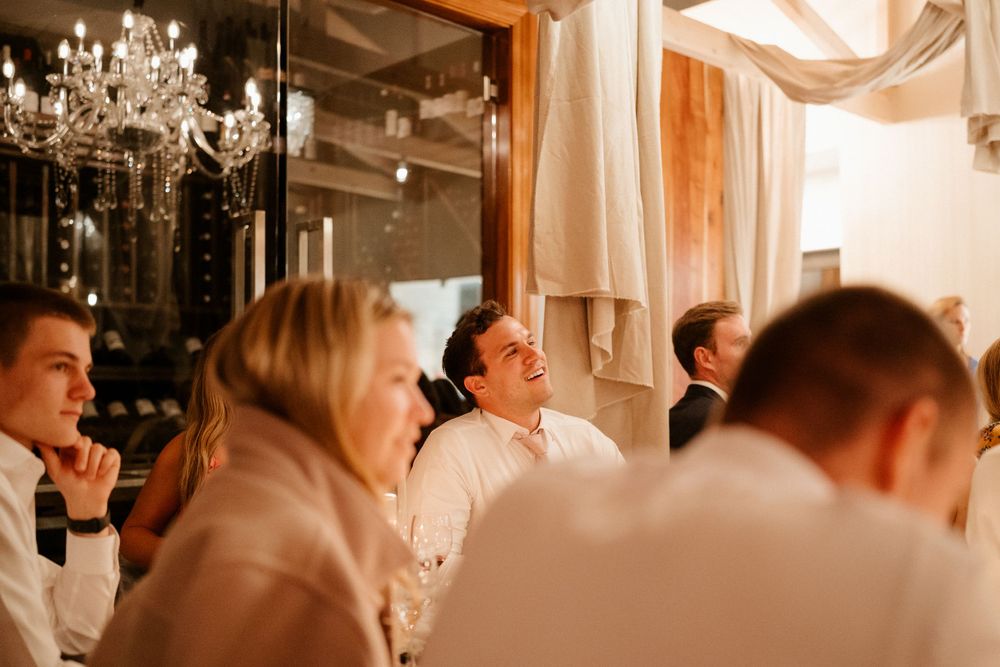Wedding reception guests gather under elegant chandeliers in warm-toned evening lighting.