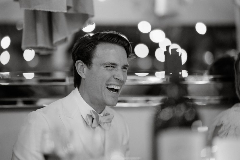 A black and white photo showing a joyful laugh during a reception with bokeh lights in the background.