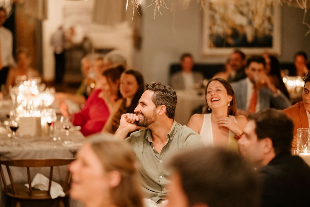 Wedding guests laugh and enjoy themselves at a candlelit reception dinner.