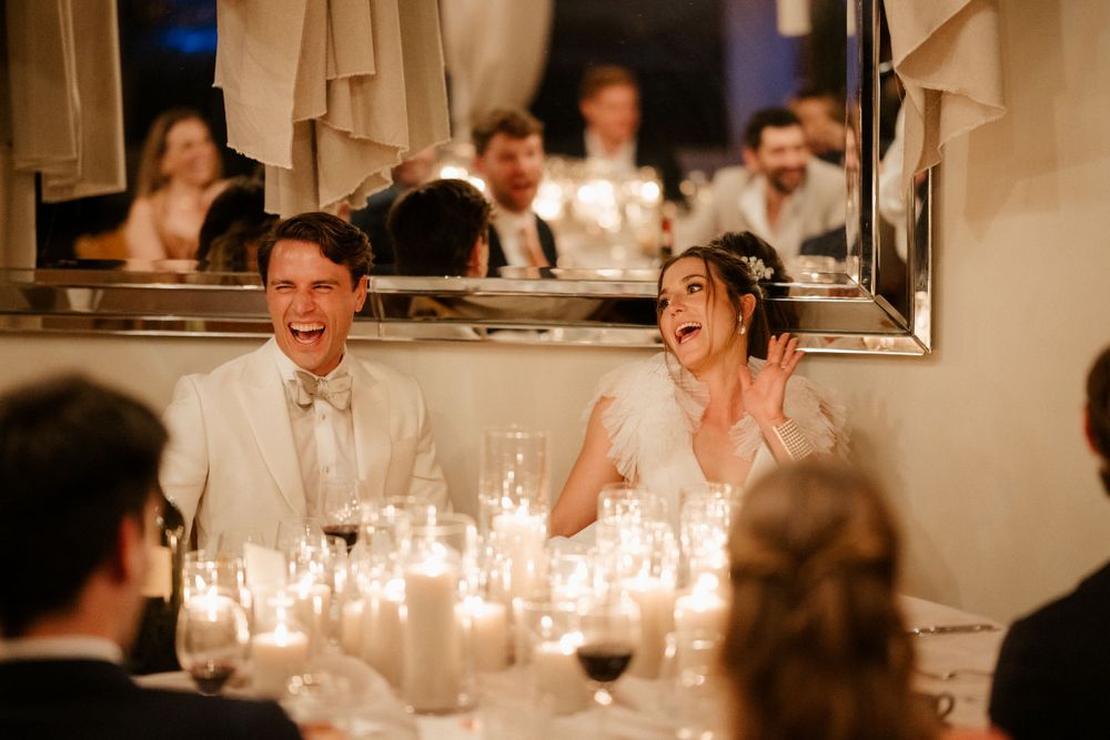 Candlelit wedding reception with guests sharing laughter around the dinner table.