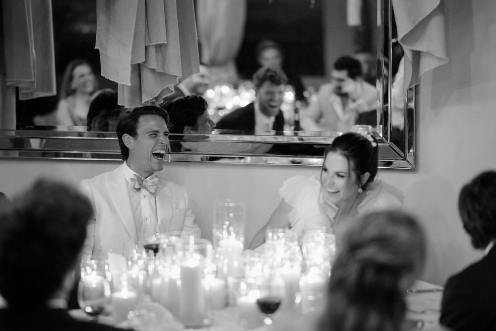 A black and white candlelit wedding reception scene showing guests enjoying the celebration.