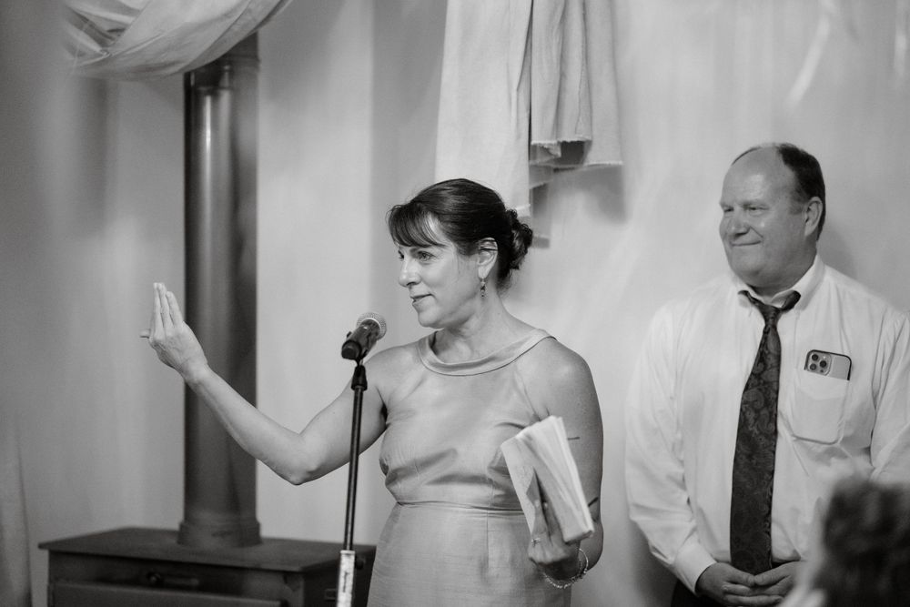 A speaker addresses wedding guests during a reception speech while holding papers.