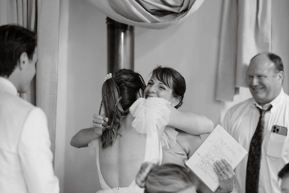 An emotional moment during a wedding ceremony with guests embracing amid white decorations.