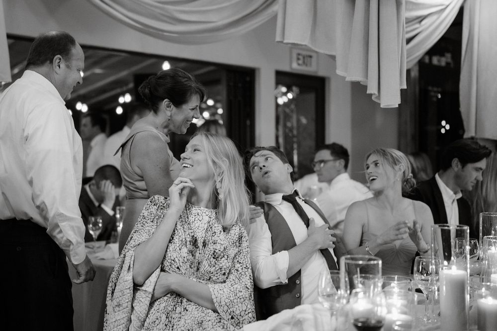 Black and white photo captures lively moments between guests during wedding reception celebration.