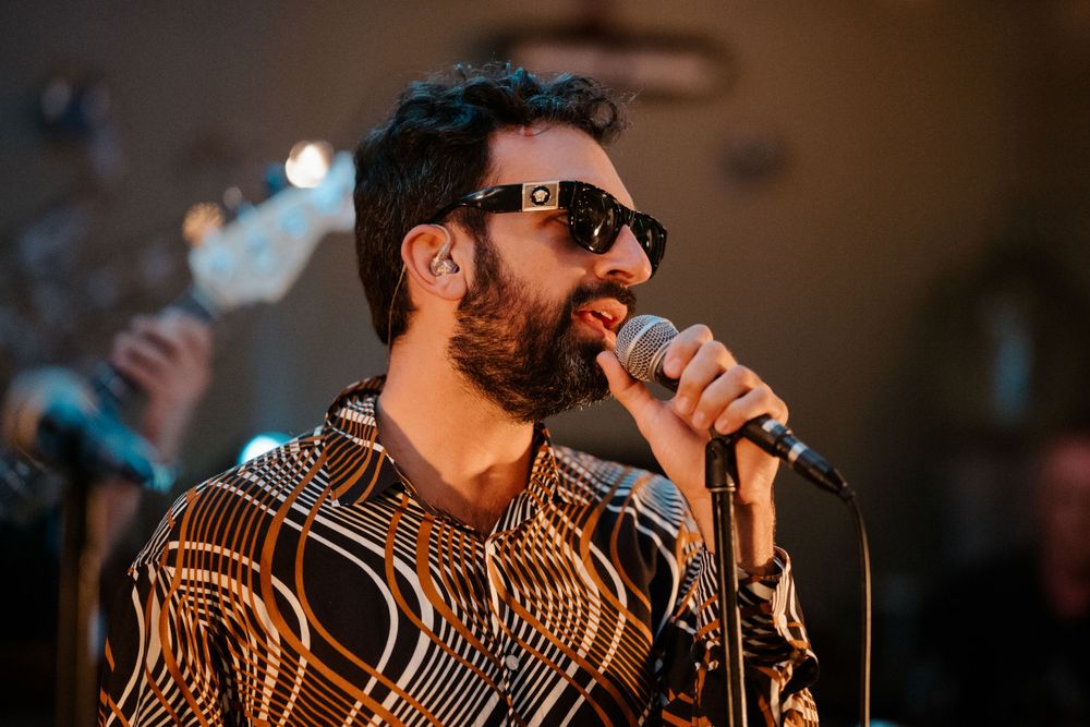 Performer in a patterned shirt singing into microphone on stage.