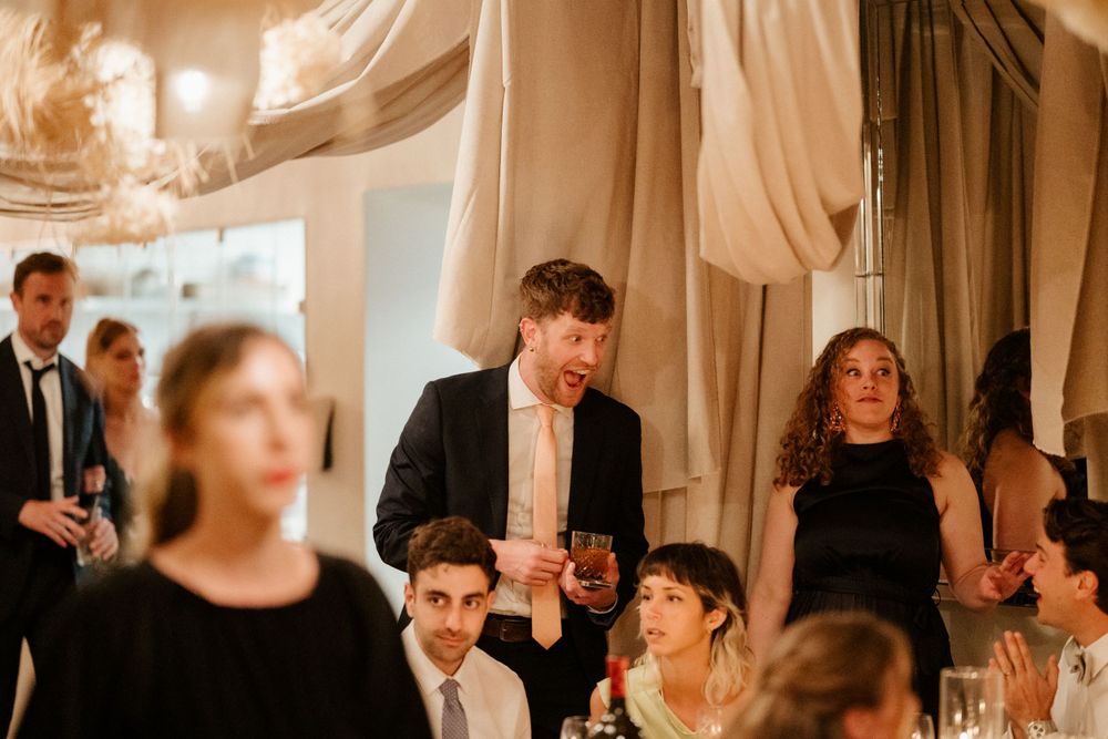Wedding reception guests gathered in an elegantly decorated room with flowing fabric drapes and warm lighting.