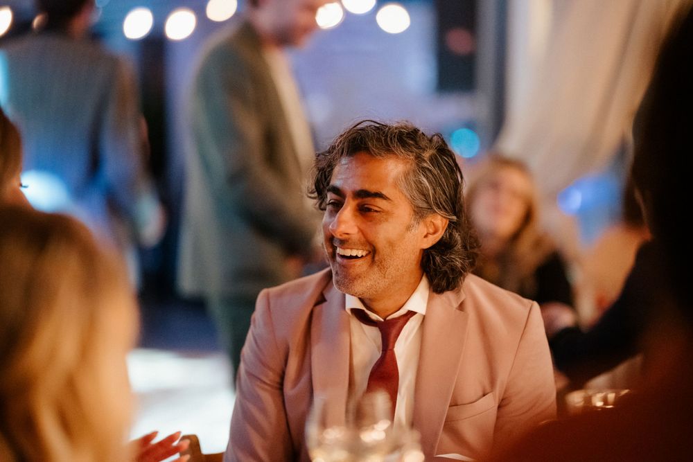 A guest in a pink suit jacket laughing during an evening wedding reception.