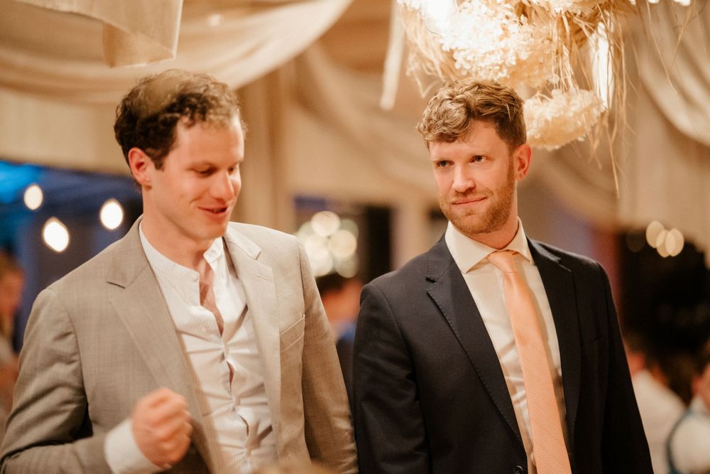 Two wedding guests in formal attire having an animated conversation at an indoor reception.
