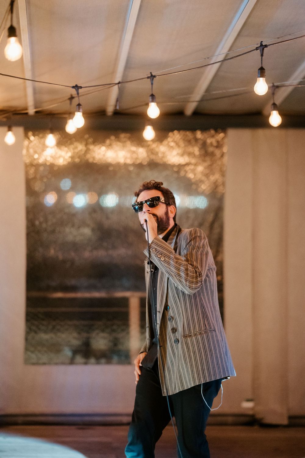 Singer performing under string lights in a venue with industrial-modern decor.