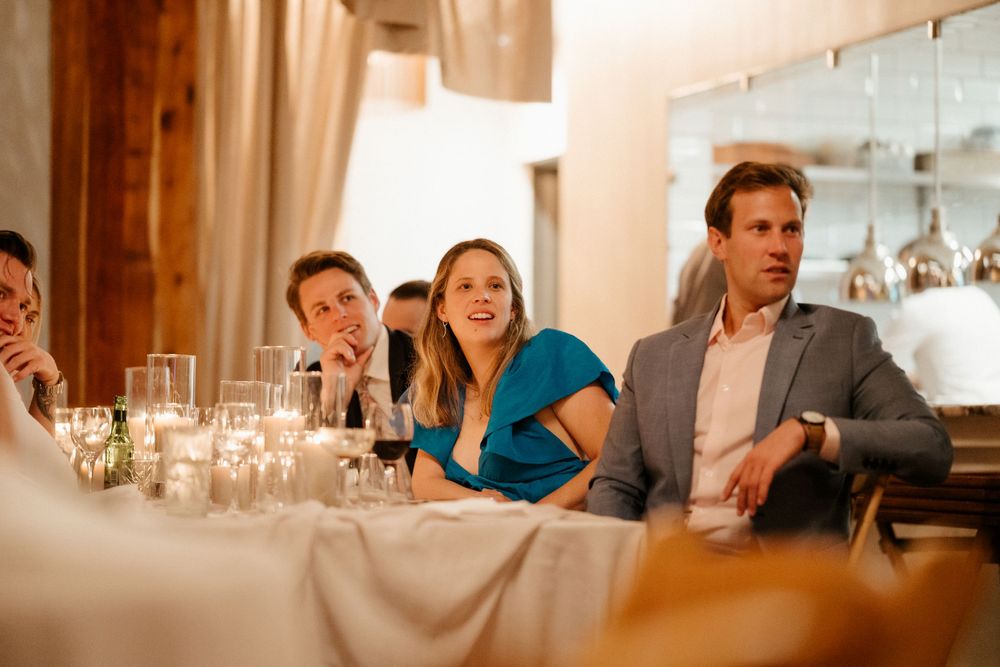 Wedding guests laughing at a reception dinner table with candlelight.