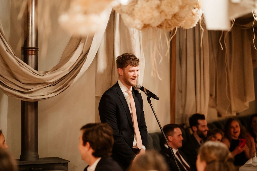 Wedding guest delivering heartfelt speech at decorated indoor reception venue.