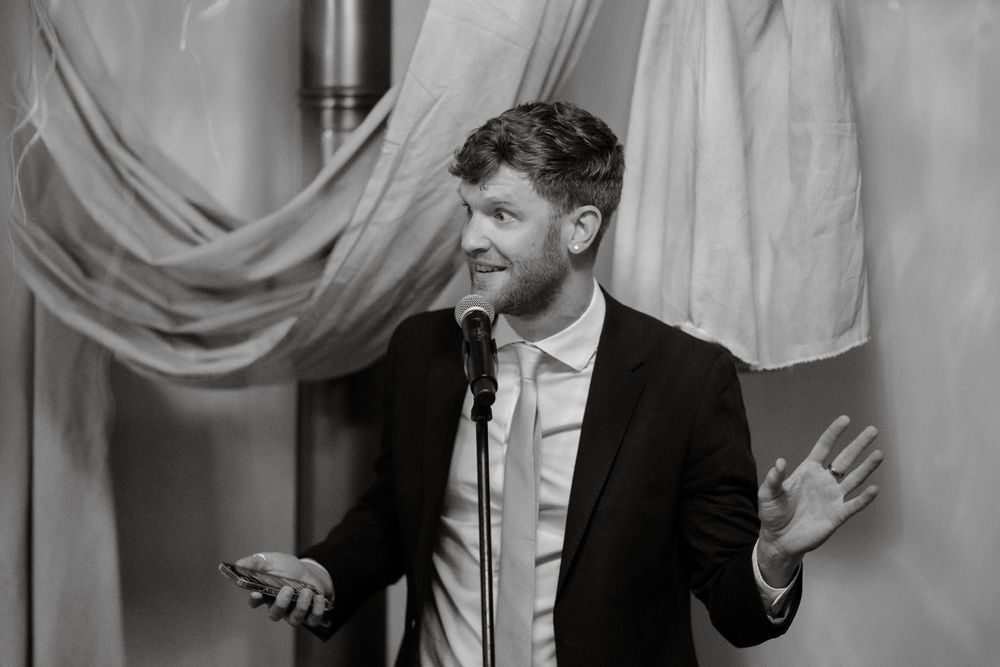 Black and white candid shot of wedding speech with expressive gestures.