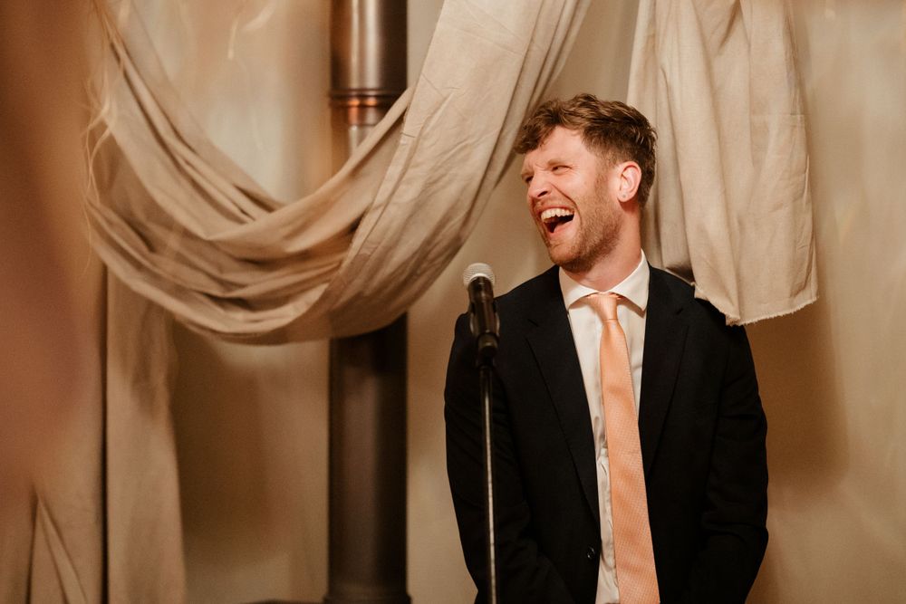 Wedding speaker delivering a joyful speech in front of elegant draped fabric decor.