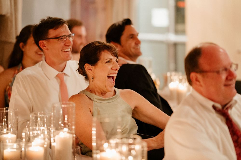 Wedding guests sharing laughs at candlelit reception dinner table.