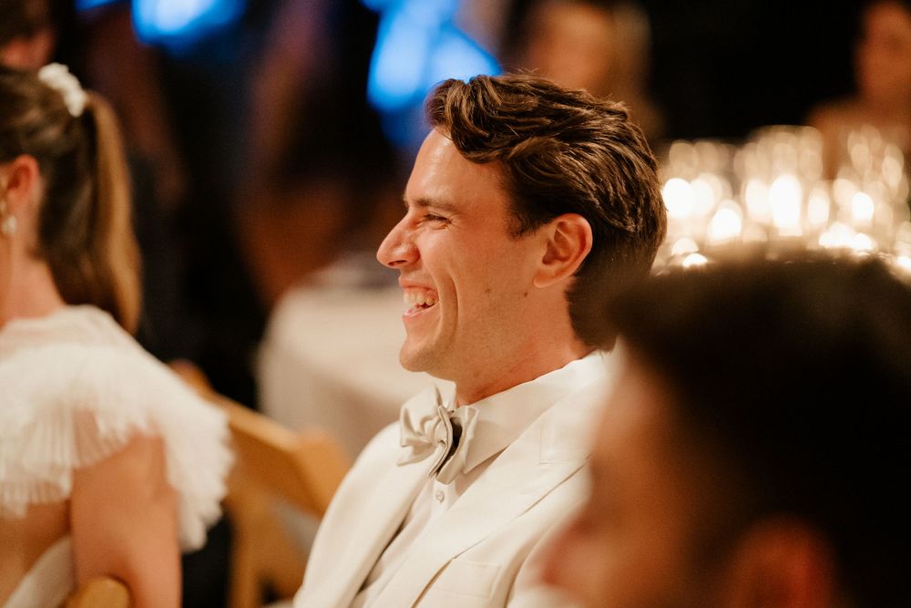 Guest smiling during wedding reception dinner under ambient lighting.
