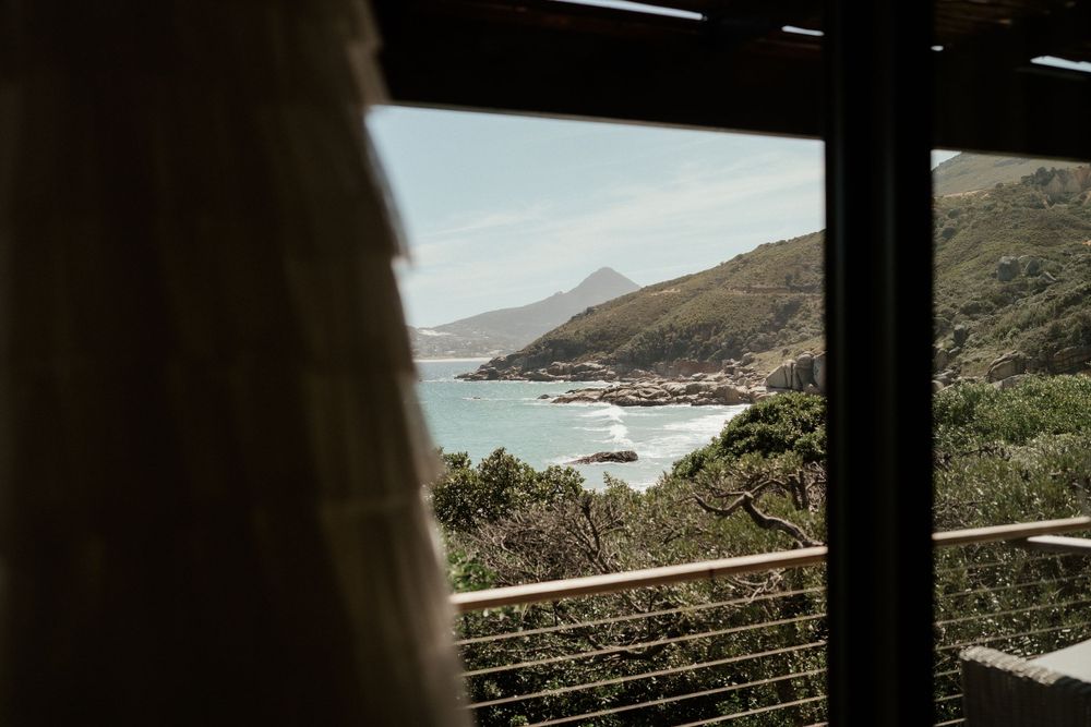 Coastal view through a window frame shows mountains meeting the ocean in the distance.