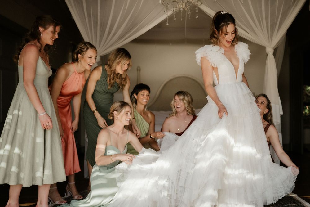 Wedding party admires bride's flowing dress during intimate indoor gathering.