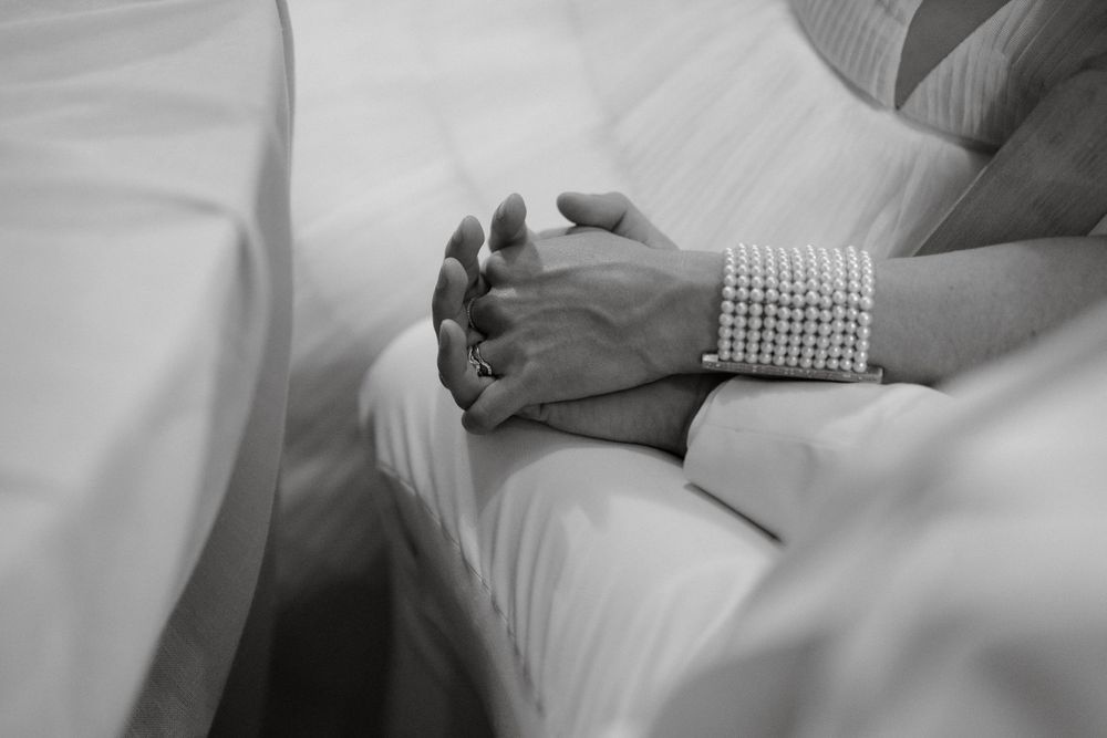 Close-up shot of clasped hands with a pearl bracelet against white fabric.