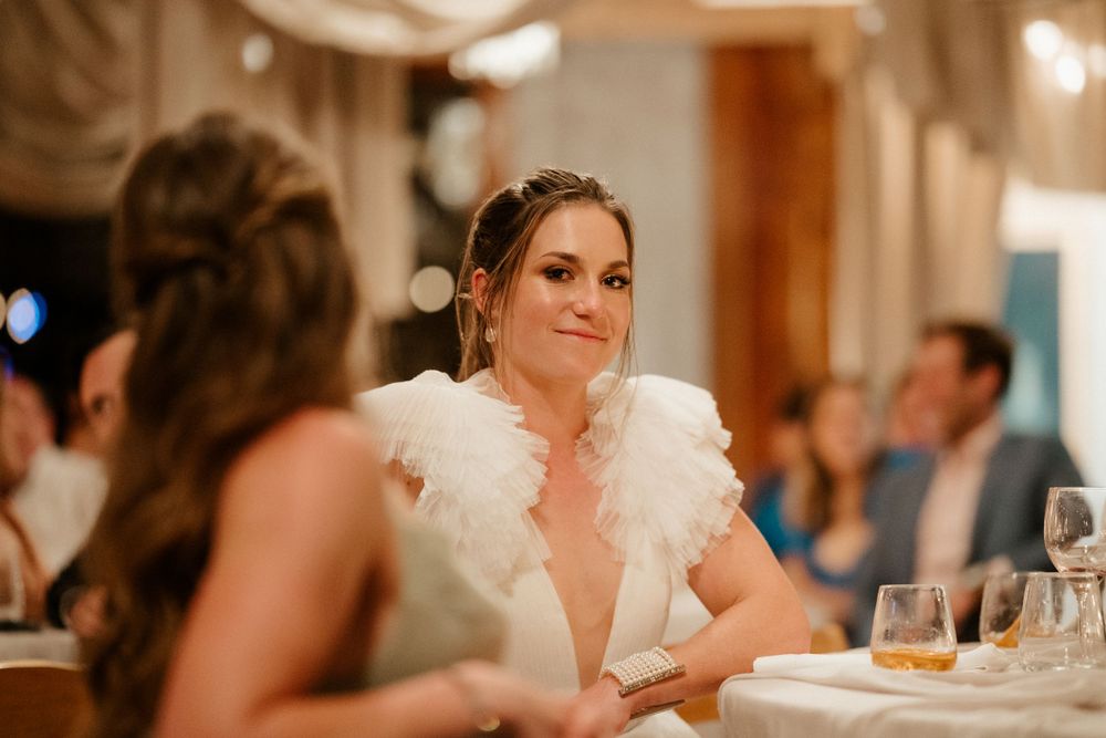 Bride in a feathered white gown sits at an elegant reception table.