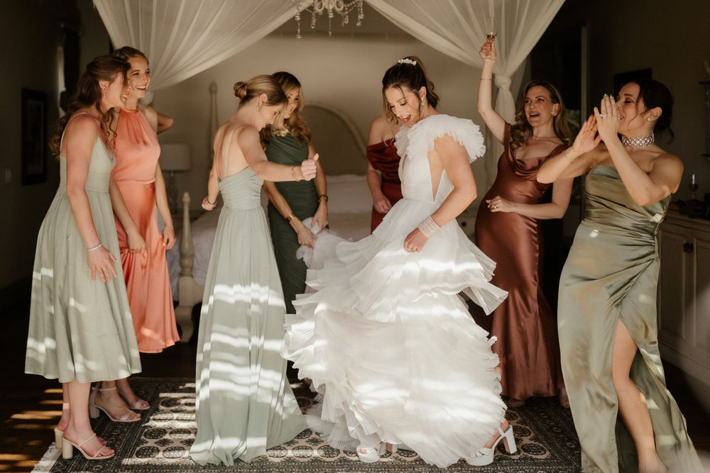 Wedding party attendees help adjust the bride's flowing white dress in an elegant indoor venue.