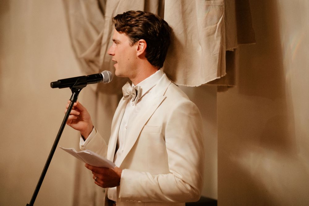Person in white suit giving speech at formal event with microphone.