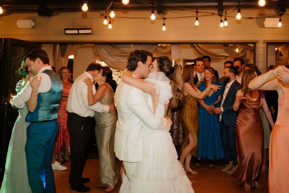 Wedding couples and guests dancing together at reception with colorful formal attire.